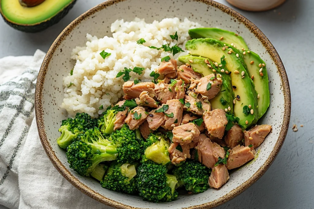 Broccoli Avocado Tuna Bowl with steamed broccoli, diced avocado, and tuna garnished with sesame seeds and parsley.