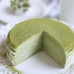 Delicious matcha crepe roll cake topped with cream and matcha powder.