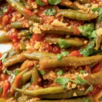 Bowl of braised pole beans in smoky tomato sauce garnished with herbs.