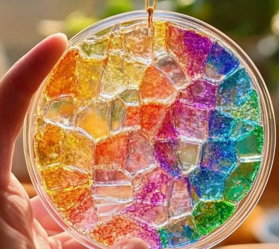 Colorful mosaic suncatcher craft using clear glue and various materials.